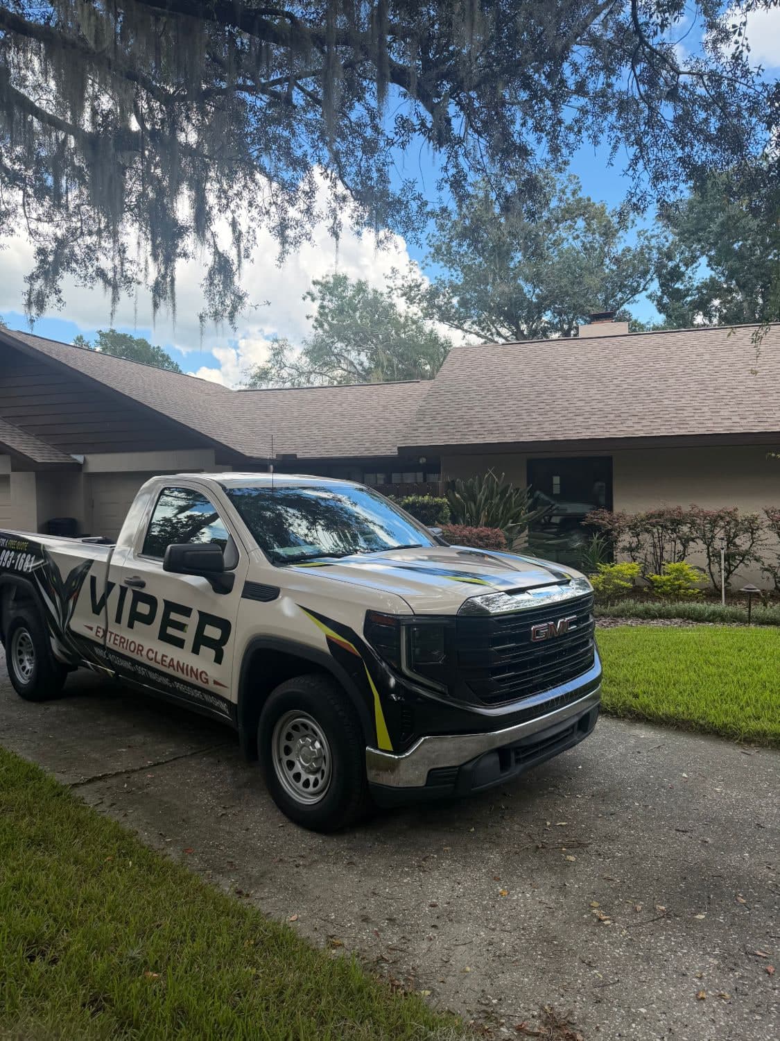 The wrapped white-and-black Viper Exterior Cleaning GMC Sierra parked in a sunny Florida driveway under a live oak